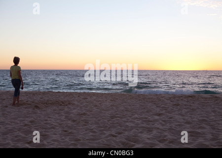 Une femme d'âge moyen les promenades le long de la plage au coucher du soleil sur la plage de la ville de Perth. Banque D'Images