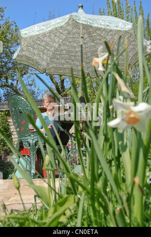 Heureuse dame senior lisant dans Sunny Garden à Pâques avec parasol Banque D'Images