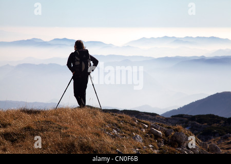 Femme alpiniste se reposant sur des bâtons de randonnée et regardant les collines environnantes. Banque D'Images