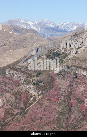 VUE AÉRIENNE.Roche sédimentaire rouge (pélite) au premier plan avec les sommets enneigés des Alpes du Sud.Alpes-Maritimes, France. Banque D'Images