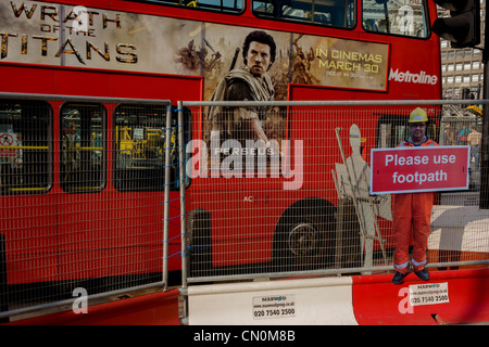 Passant red bus avec la colère des Titans film annonce et les droits de l'échelle figure workman qui avertit les piétons à rester sur sentier, et ne pas vous promener dans le site de construction des routes. Banque D'Images
