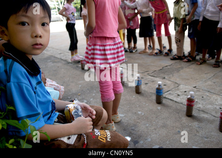 Un garçon qui est un étudiant de l'école est assis à proximité d'enfants jouer à un jeu à l'École d'Angkor à Kampong Cham, au Cambodge. Banque D'Images