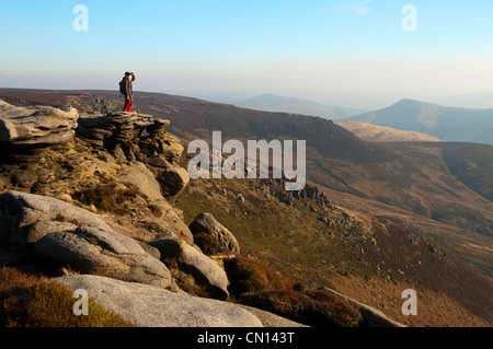 Un marcheur se dresse sur le bord de la Kinder Scout plateau au-dessus de Edale, Peak District, Derbyshire, Angleterre, Royaume-Uni. Banque D'Images