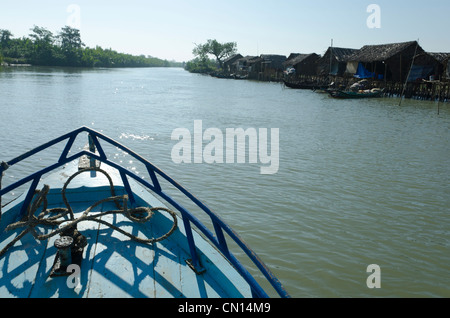 Bateau naviguant sur la voie navigable avec des huttes de bambou dans le delta de l'Irrawaddy. Le Myanmar. Banque D'Images