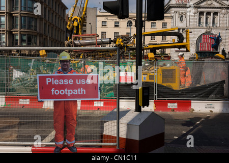 Les travailleurs de la construction réelle dans l'arrière-plan et une figure de l'ouvrier qui met en garde les piétons à rester sur sentier, et ne pas vous promener dans le site de construction de la route lorsque l'amélioration des rues à Victoria, au centre de Londres. Banque D'Images