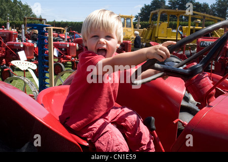 Ecstatic petit garçon vêtu de rouge, 'attelage' un tracteur rouge vif ! Banque D'Images