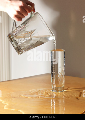 On verse de l'eau d'une cruche dans un verre et ses débordements Banque D'Images