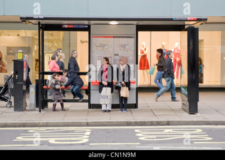 Oxford Street West End de Londres deux jeunes filles ethniques mesdames femmes femelles avec les enfants attendent en abribus pour le bus Banque D'Images