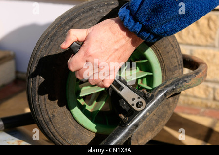 Un homme utilise une clé à douille pour déposer la roue d'une brouette de jardin Banque D'Images