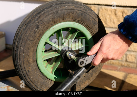 Un homme utilise une clé à douille pour déposer la roue d'une brouette de jardin Banque D'Images