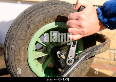 Un homme utilise une clé à douille pour déposer la roue d'une brouette de jardin Banque D'Images