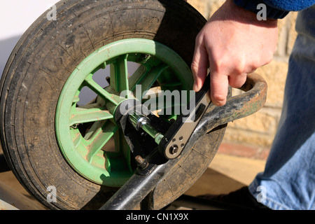 Un homme utilise une clé à douille pour déposer la roue d'une brouette de jardin Banque D'Images