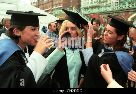 Une femme diplômée en toge et mortier bord fête son diplôme avec une bouteille de bière Banque D'Images