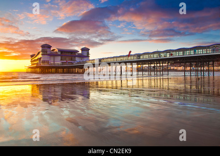 Coucher de soleil sur la grande jetée à Weston-Super-Mare, Somerset, England, UK compte dans le sable humide de la plage à marée haute. Banque D'Images