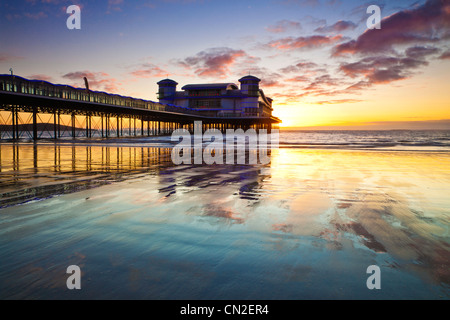 Coucher de soleil sur la grande jetée à Weston-Super-Mare, Somerset, England, UK compte dans le sable humide de la plage à marée haute. Banque D'Images