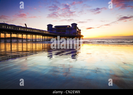 Coucher de soleil sur la grande jetée à Weston-Super-Mare, Somerset, England, UK compte dans le sable humide de la plage à marée haute. Banque D'Images