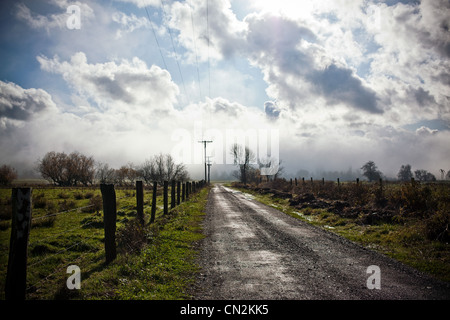 Chemin rural avec clôture et nuages dans le ciel Banque D'Images