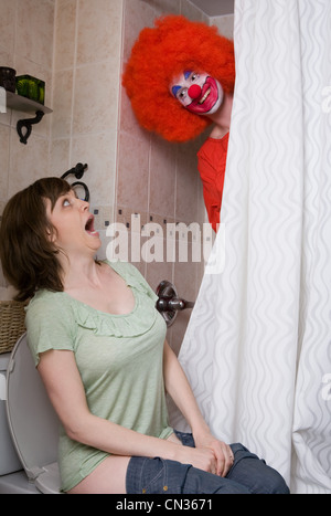 Clown d'effrayer une femme sur les toilettes Banque D'Images