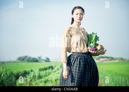 Young woman holding basket dans le champ de légumes cultivés sur place Banque D'Images