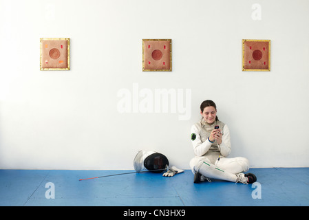 Escrimeur féminin sitting on floor using cell phone Banque D'Images