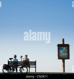 Vue arrière d'un couple d'âge moyen assis sur un banc au bord de la mer, sur un après-midi de printemps, Aberaeron Ceredigion Pays de Galles UK Banque D'Images