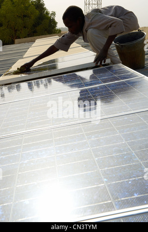 Jeune garçon nettoie la poussière de panneaux solaires en Afrique Banque D'Images