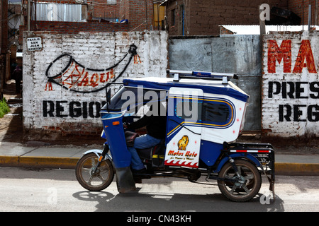 Taxi tricycle motorisé (mototaxi) passant par l'insigne du parti politique et la propagande peinte sur le mur, Puno, Pérou Banque D'Images