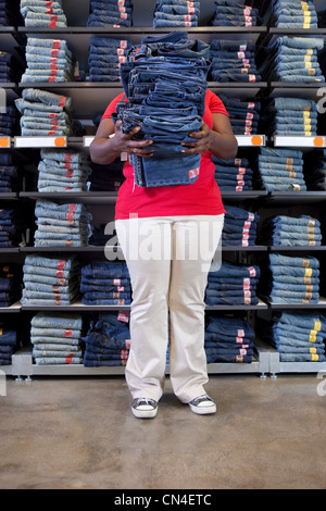 Young woman carrying pile de vêtements en jeans store Banque D'Images