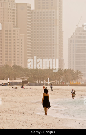 Une femme en robe noire, de la marche sur la plage, la Marina de Dubaï, Dubaï, Emirats Arabes Unis vue arrière. Banque D'Images