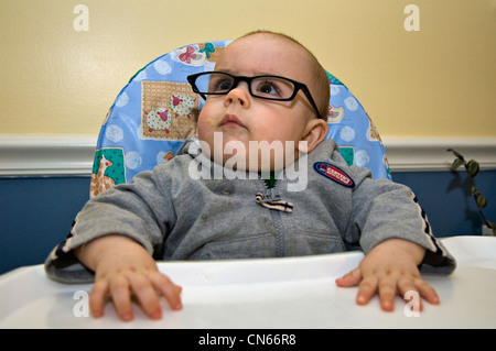 9 mois, malpropre Baby Boy Wearing Glasses dans une chaise haute Banque D'Images