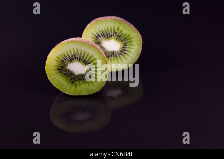 L'Actinidia deliciosa. Les kiwis cross section réfléchi sur une surface noire. Groseille de Chine. Banque D'Images