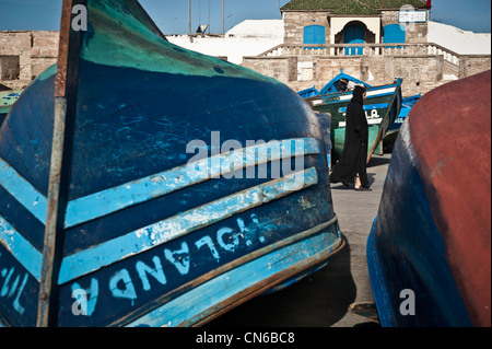 Homme marchant local entre les bateaux de pêche du port d'Essaouira, Maroc. Banque D'Images