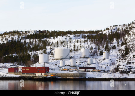 Une installation de stockage de pétrole sur les rives d'un fjord avec une montagne couverte de neige derrière prises au format paysage Banque D'Images