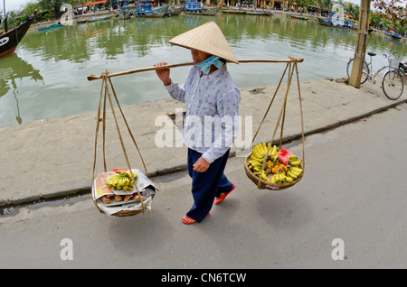 Femme portant des paniers de fruits de la chape dans street, Hoi An, Vietnam Banque D'Images