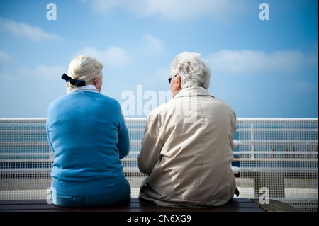 Vue arrière de deux personnes âgées retraitées assis sur un banc sur la promenade d'Aberystwyth, chaud après-midi de printemps, le Pays de Galles UK Banque D'Images