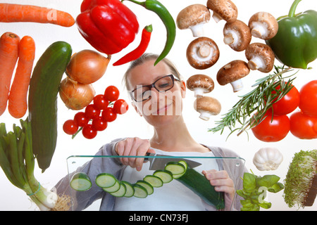 Jeune femme est hacher les légumes dans une cuisine. Vu à travers une table en verre. Banque D'Images