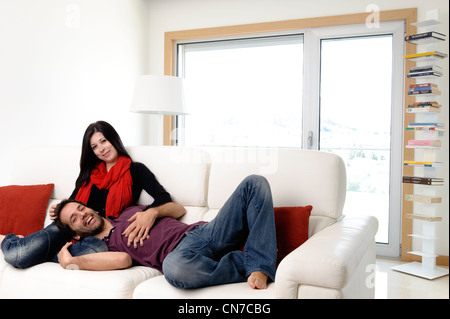 Happy young couple at home dans le salon assise sur un canapé blanc Banque D'Images