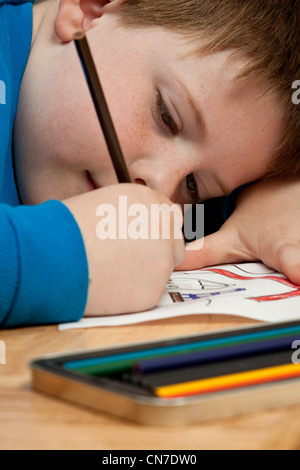 Jeune garçon en chemise bleue en coloriant un dessin avec des crayons tout en jetant sur le sol. Banque D'Images