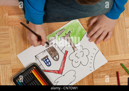 Jeune garçon en chemise bleue en coloriant un dessin avec des crayons tout en jetant sur le sol. Banque D'Images