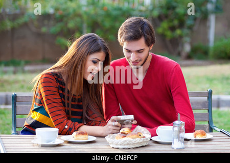 Young couple having coffee à une table d'extérieur affichage des photographies sur le dos d'un appareil photo numérique compact Banque D'Images