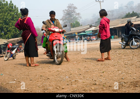 Un homme sur une moto Honda rouge est en train de parler à deux femmes des tribus des collines près de la route principale à Pang Ma Sappong (Pha) en Thaïlande. Banque D'Images