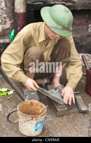 L'homme à l'aide d'une pierre à aiguiser une lame dans la vieille ville, Hanoi, Vietnam Banque D'Images