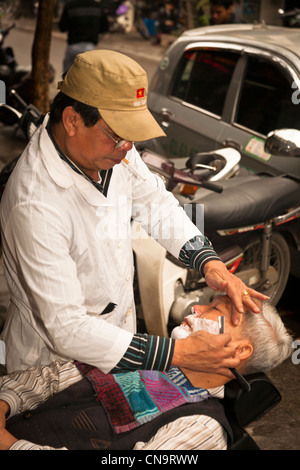 Un salon de coiffure le rasage un homme dans la rue dans la vieille ville, Hanoi, Vietnam Banque D'Images