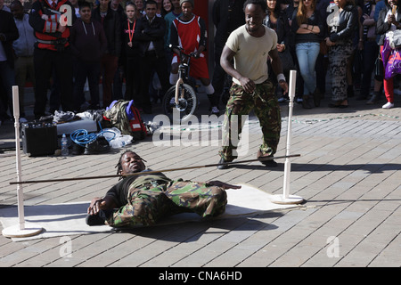 Des artistes de rue danse limbo sous un poteau avec un public d'observer les gens dans le centre-ville de Leeds Yorkshire Angleterre UK Banque D'Images