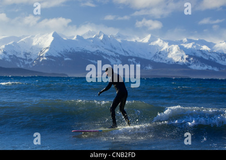 Homme surf le long de la côte en hiver avec gamme Chilkat dans l'arrière-plan, Eagle Beach, sud-est de l'Alaska Banque D'Images