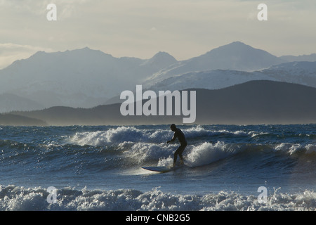 Homme surf le long de la côte en hiver avec gamme Chilkat dans l'arrière-plan, Eagle Beach, sud-est de l'Alaska Banque D'Images