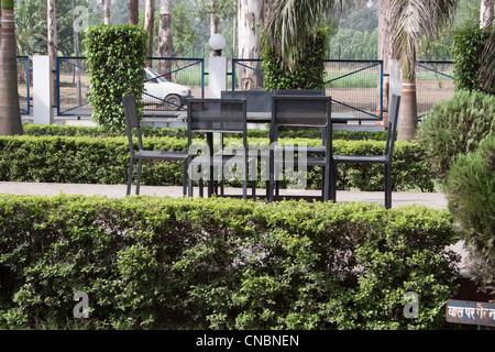 Quelques chaises et une table en pierre dans le jardin de la Monty Millions restaurant près de Meerapur, avec de nombreux arbustes et arbres Banque D'Images