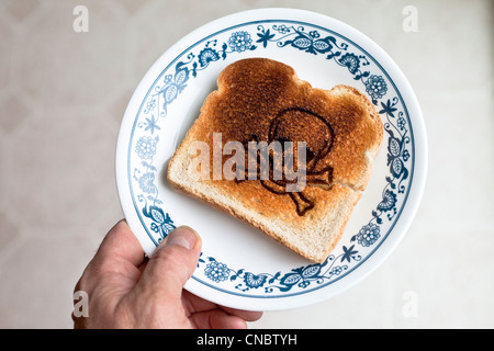 Crâne et os croisés brûlé dans un morceau de pain grillé sur une plaque allergie au gluten la maladie cœliaque. Banque D'Images