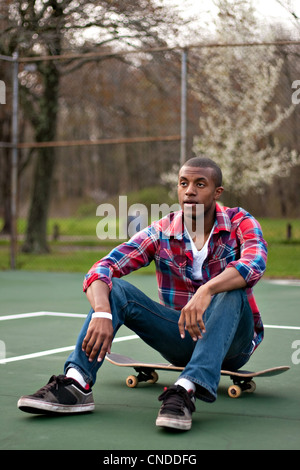 Un jeune homme de traîner dans le tennis assis sur sa planche à roulettes. Banque D'Images