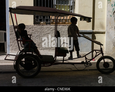 Deux jeunes garçons âgés de 5-6 cubains jouent sur un pedicab c'est garée dans la rue à La Havane, Cuba. Banque D'Images